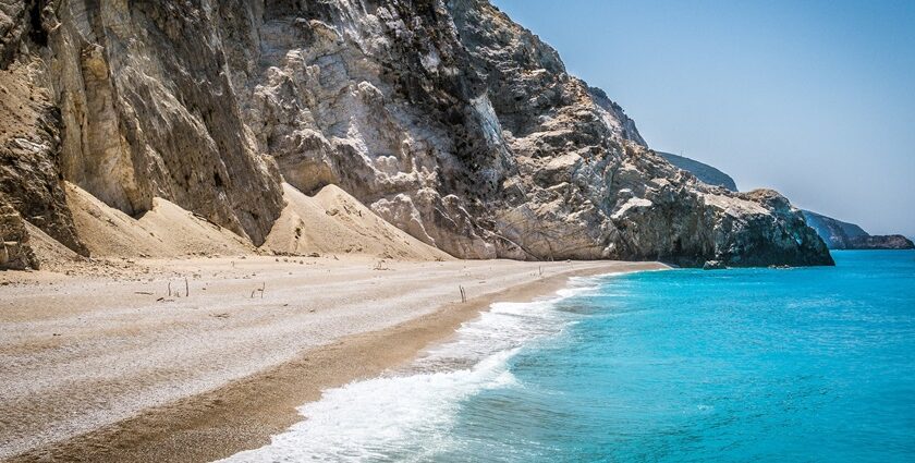 A beautiful beach scene with clear blue water, soft white sand, and a vibrant green island in the background.