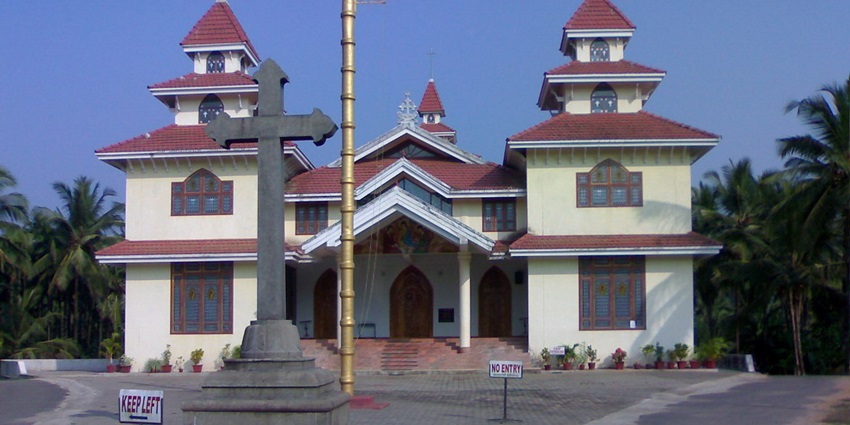 Colonial-era Catholic church in Belthangady with tall steeple, stained glass windows, and peaceful courtyard surrounded by lush greenery.