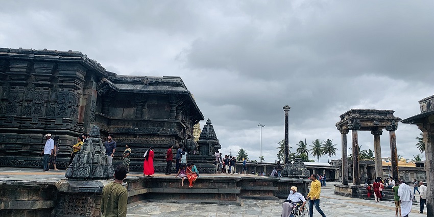 A temple complex with intricate carvings and people walking around under a cloudy sky