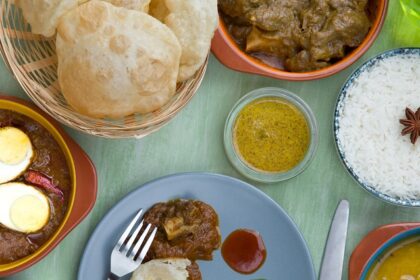 An image of dishes cooked in Maharashtrian style from Pune, like rice, dal, egg gravy, puri, etc.