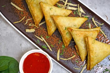 Five triangular-shaped snacks served on a black tray accompanied by a red dip