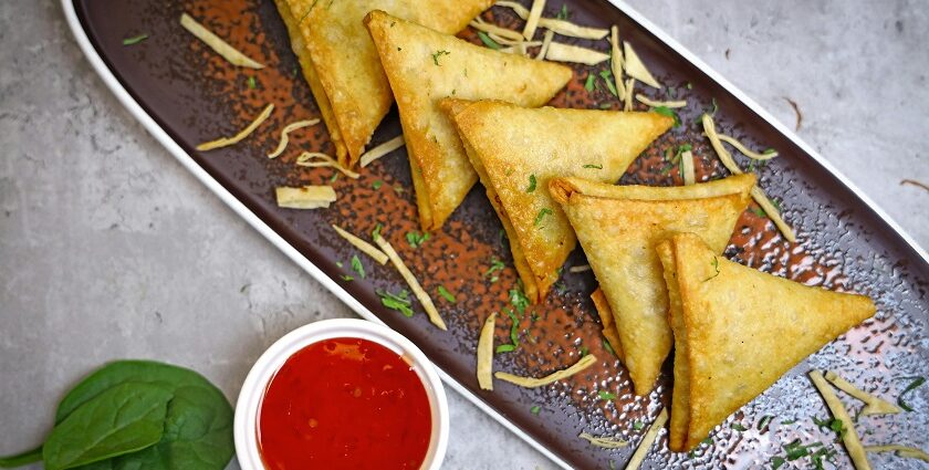 Five triangular-shaped snacks served on a black tray accompanied by a red dip