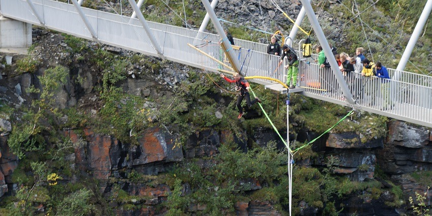 A bungee jumper leaping from Gorsabrua Bridge, with others waiting with the instructor