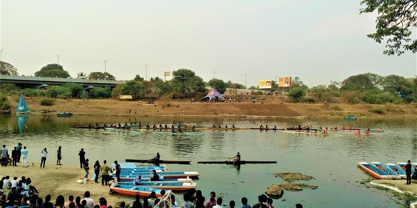 Rowing boats arranged in an arrow formation on a river in Pune, crowded by tourists.