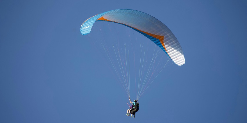 Paraglider and operator standing on hill preparing for takeoff with a colourful parachute.