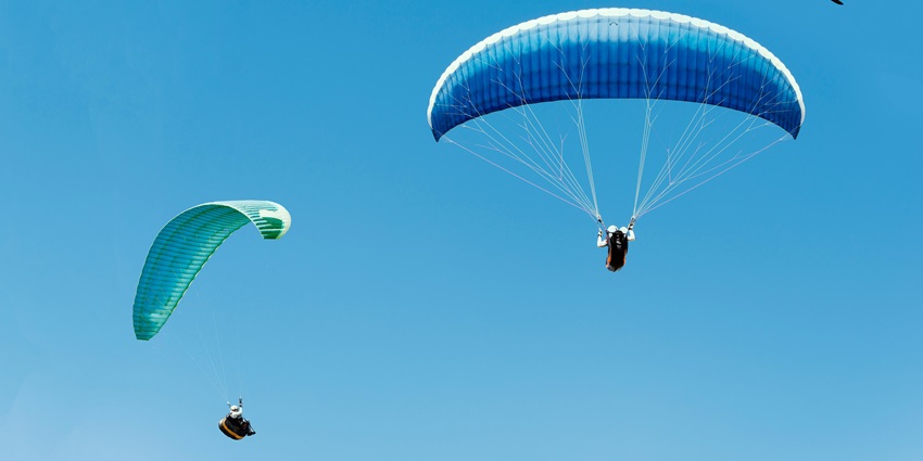 Multiple solo paragliders floating in the clear blue sky with nothing else in view.