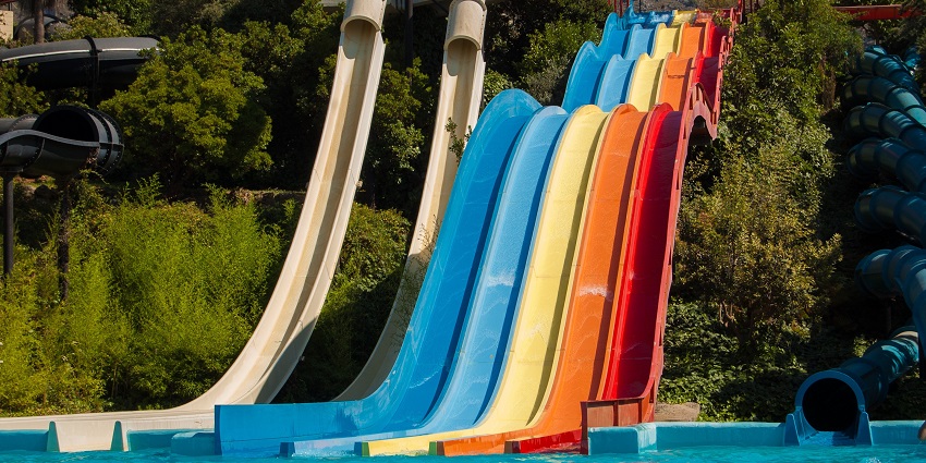 A colourful water slide at a water park on a sunny day, surrounded by a clear blue sky and trees