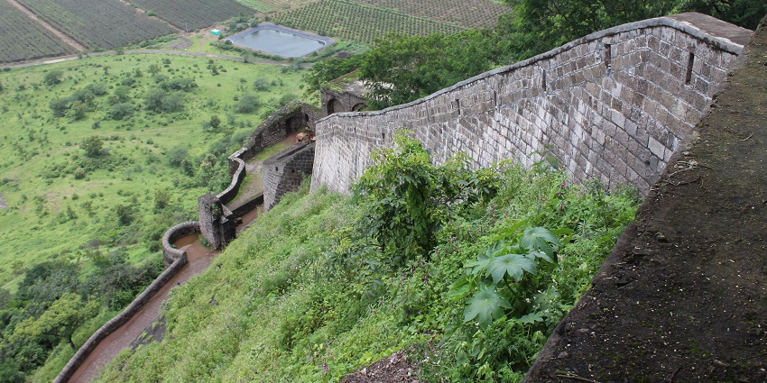 Image of an ancient fort on top of the hill surrounded by lush greenery and greenfield