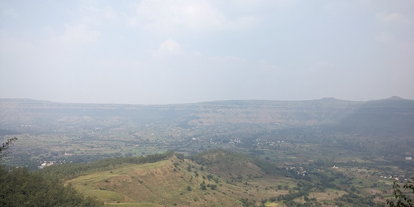 A view of Sajjangad Fort's stone pathways with green hills and mist in the background.