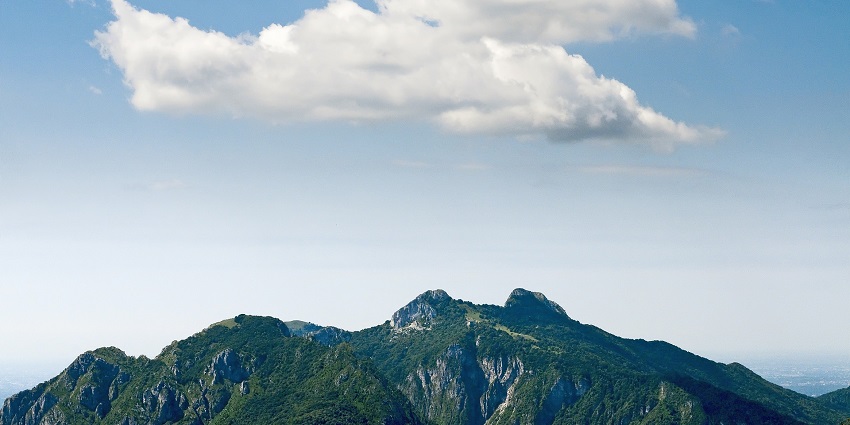 Mountain peaks rising into a blue sky, partially covered by soft white clouds.