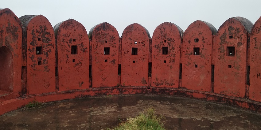 A stone bastion of Nagardhan Fort stands tall against a clear blue sky, surrounded by greenery.