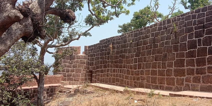 View of Bankot Fort in Maharashtra, featuring restored walls and surrounding greenery.