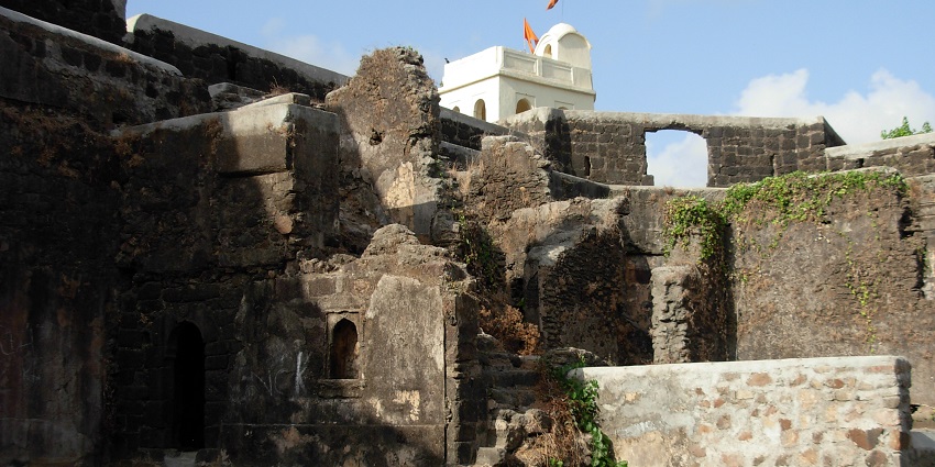 Shirgaon Fort, showcasing its ancient stone walls and fortifications surrounded by greenery under a clear sky