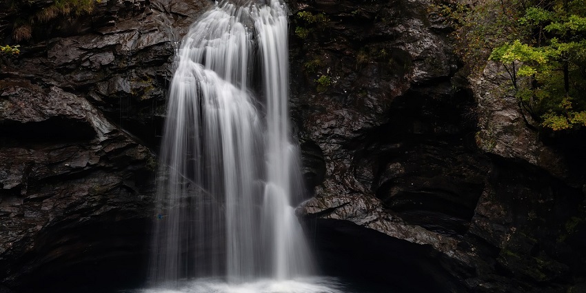 The Waghora Waterfalls cascades over rocky cliffs, surrounded by lush green foliage, creating a tranquil scene.