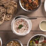 An Indian food spread consisting of a variety of curries, salad, curd, and flatbread.