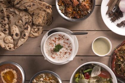 An Indian food spread consisting of a variety of curries, salad, curd, and flatbread.