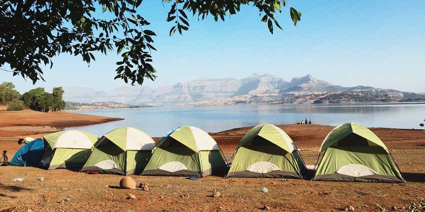 Five tents are located near the bank of a river across which there are mountains