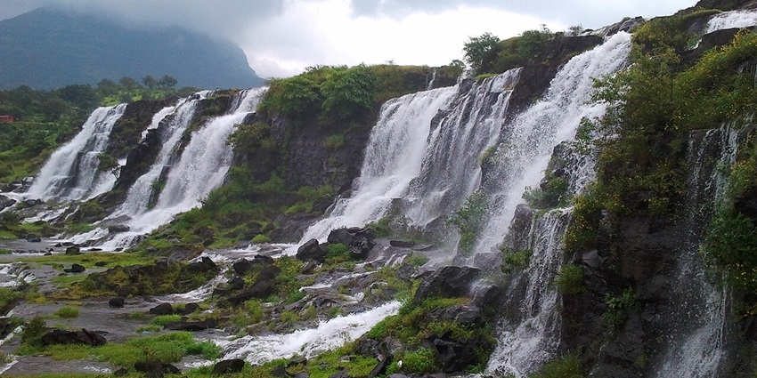 A picture of a scenic waterfall with a strong stream cascading down a rocky hill amidst lush greenery