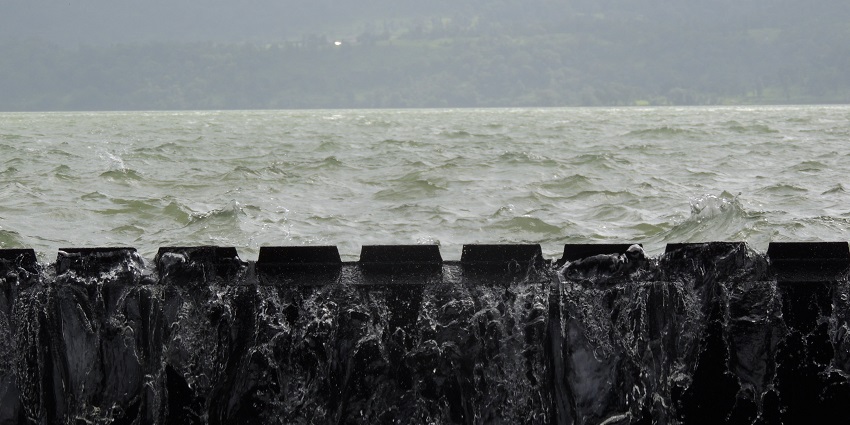 A large dam at Bhandardara, surrounded by greenery and mountains under a cloudy sky.