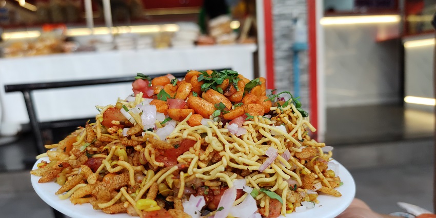 Bhel puri topped with pomegranate seeds and sev served in a bowl with different sides