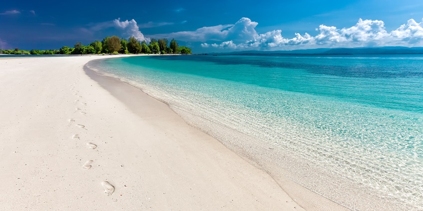 Bhatkal is a sandy beach scene with gentle waves and footprints leading towards the sea under a clear sky.