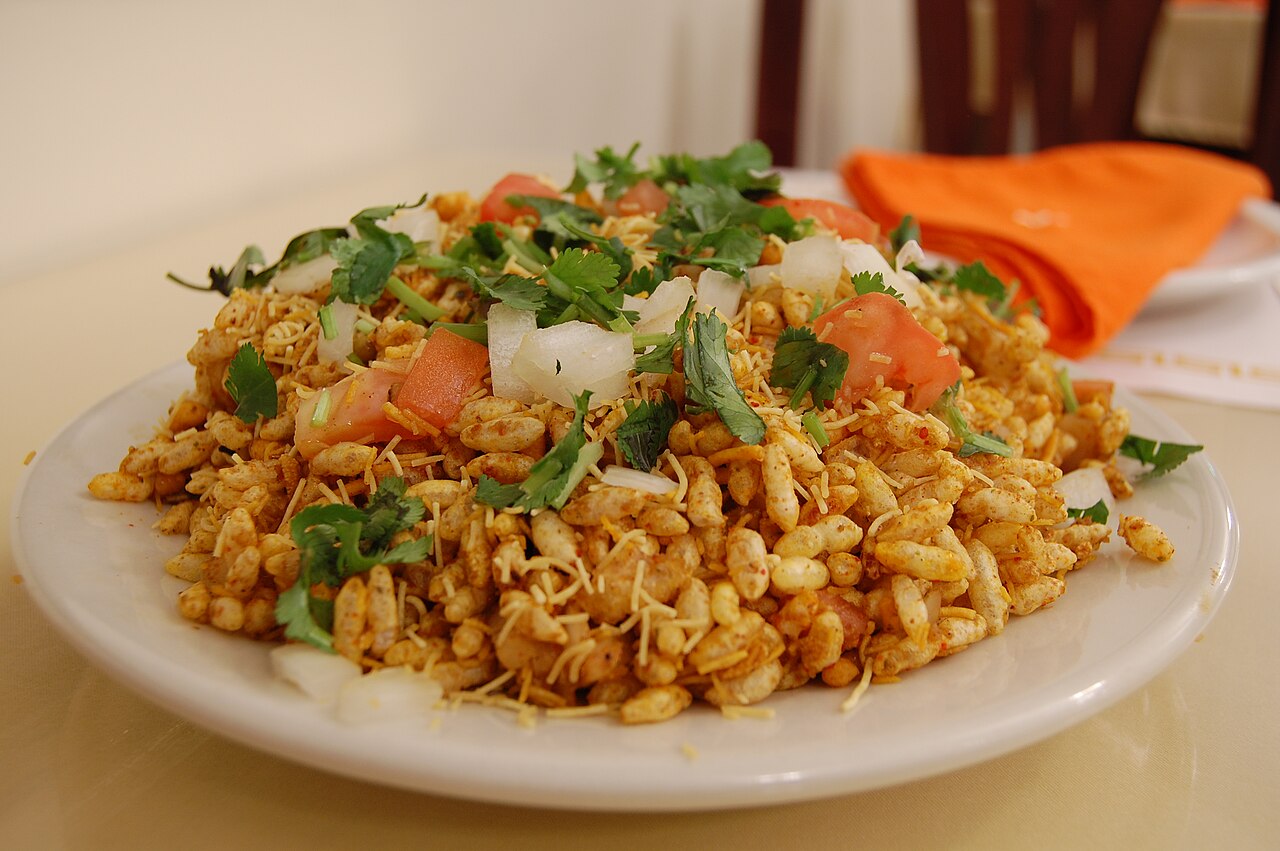 Bhelpuri topped with sev and coriander served on a white plate with a blurred background