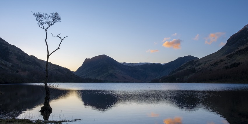 A serene morning at Lake, surrounded by lush mountains and a clear blue sky.