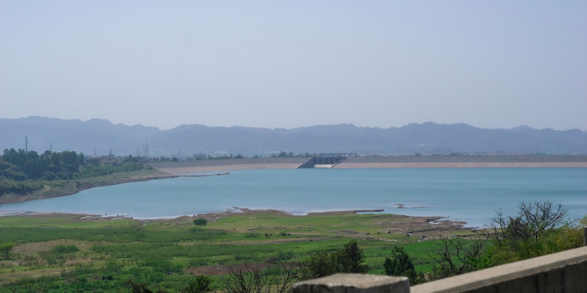 A calm view of Bhira Dam, with green hills and clear waters in the background.