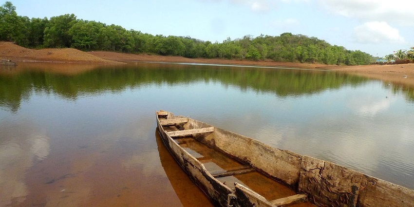 An old wooden kayak lying on the shore of the badwaters, surrounded by greenery