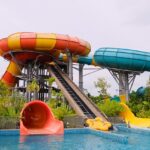 The image shows a yellow water slide curving downward into a clear blue pool in Bhor Adventure Park.