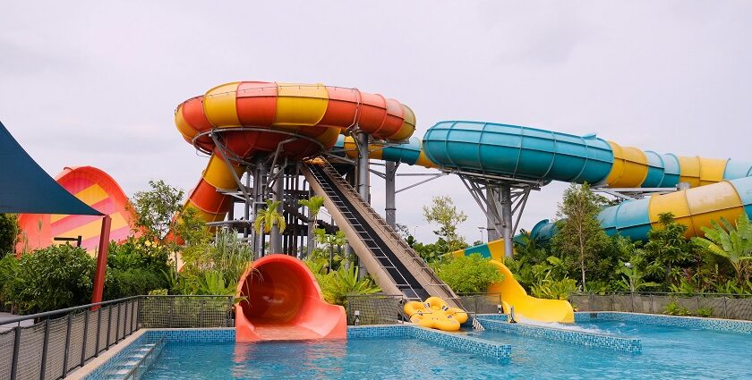 The image shows a yellow water slide curving downward into a clear blue pool in Bhor Adventure Park.