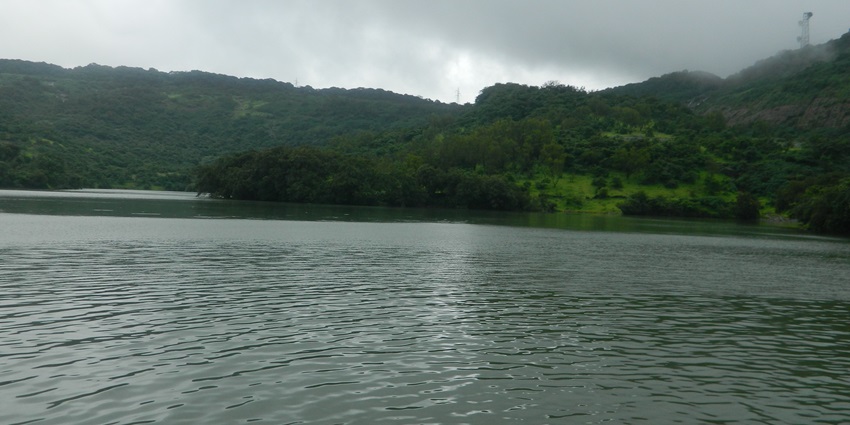 The calm waters of Bhushi Dam are surrounded by greenery and hills covered in mist in Lonavala.
