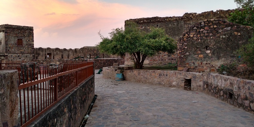 Sunset at Ranthambore Fort featuring ancient structure with greenery and rugged terrain.