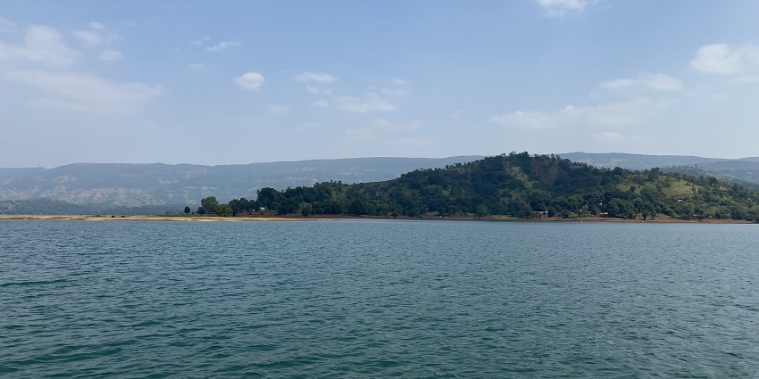 The image depicts a Shivsagar Lake, a large body of water surrounded by lush green