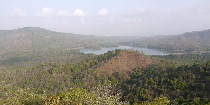 View of Tulsi Lake surrounded by greenery, with hills in the background under cloudy sky.