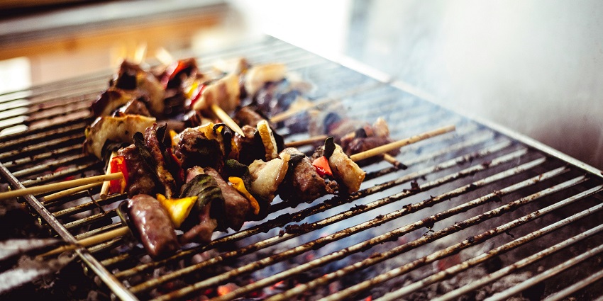 A picture of meat pieces arranged on sticks and placed on a barbeque grill.