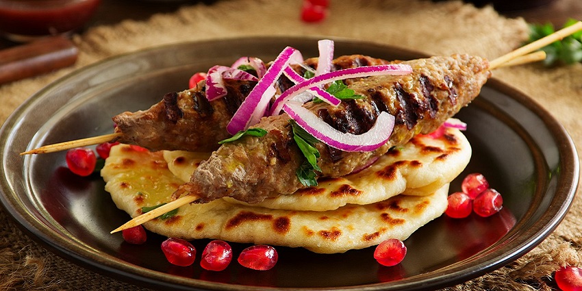 Lamb Kebab and fluffy bread, topped with sliced onions, coriander, and pomegranate seeds.