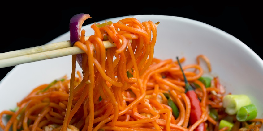 Chilli Garlic Noodles topped with fried vegetables in a bowl garnished with spring onions.