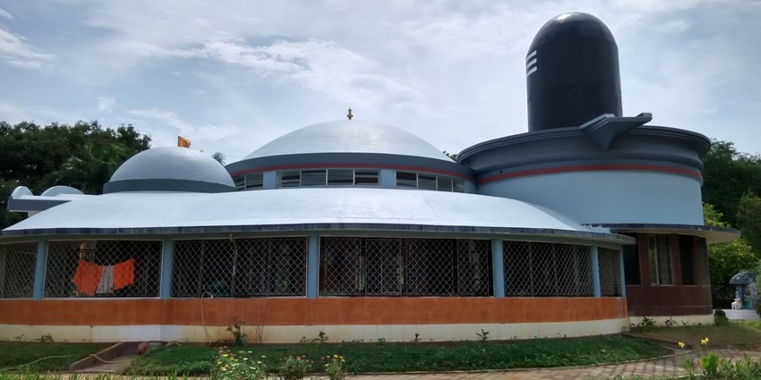 A picture of a temple built in the shape of a massive Shiva Linga, surrounded by lush greenery