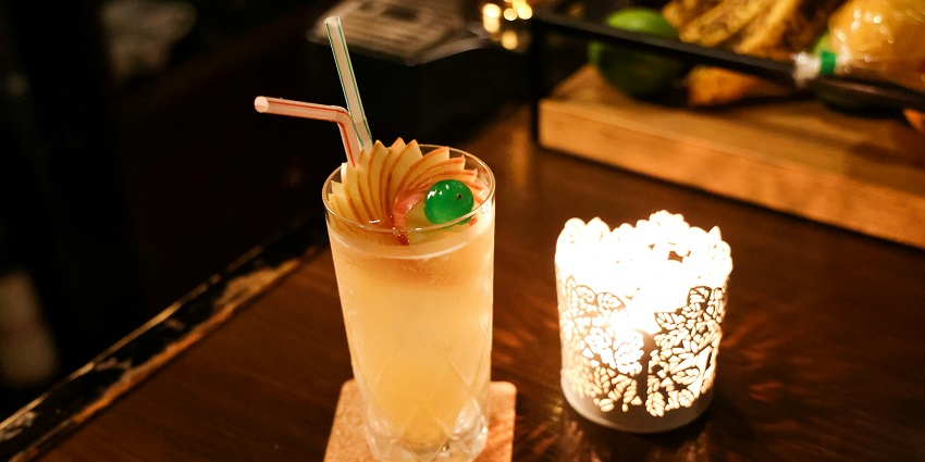 Image of a glass with drink topped with apples pieces one the other side a small table candle