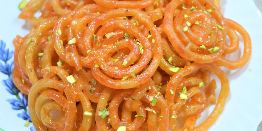 Jalebi, an Indian dessert served on a plate garnished with almonds and pistachio
