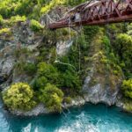 A person springing off of a bridge with a river flowing through the green valleys.