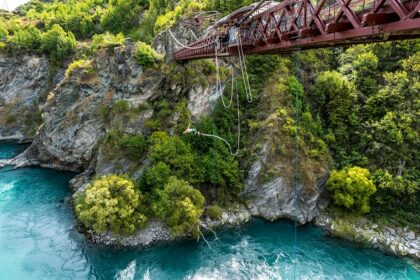 A person springing off of a bridge with a river flowing through the green valleys.