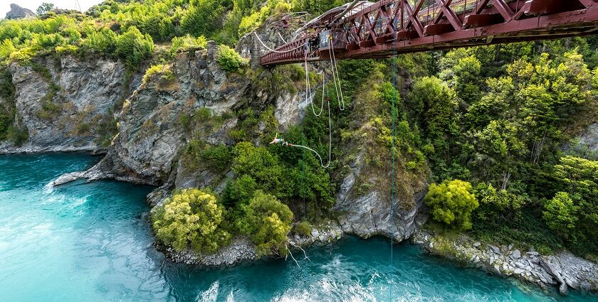 A person springing off of a bridge with a river flowing through the green valleys.