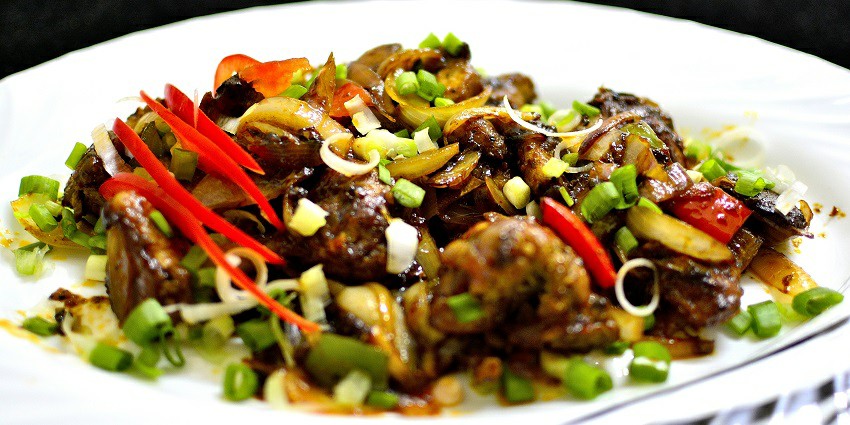 Chilli Chicken served on a plate garnished with spring onions, carrot and tomatoes