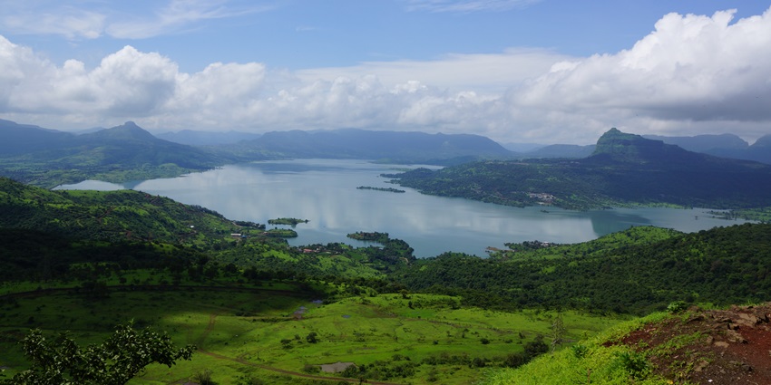Image of the tranquil Pawna lake surrounded by lush green hills under a partly cloudy sky