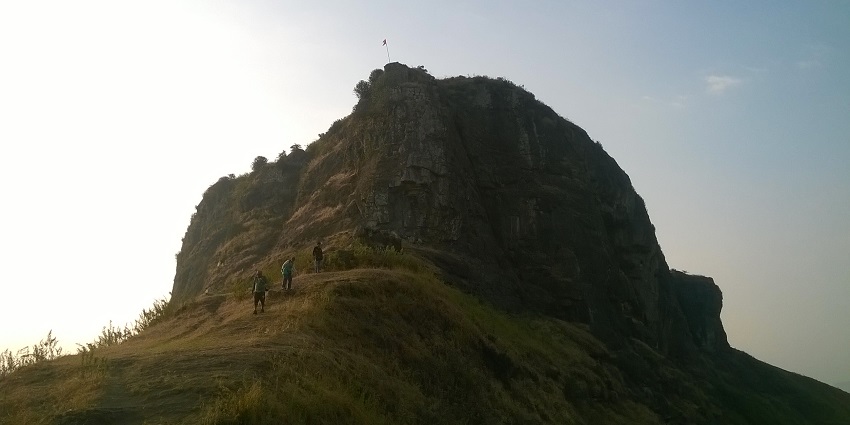 Trekkers climbing the steep slopes of the Kavnai fort on a hilltop on a clear day.