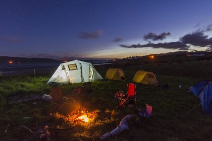 Bonfire and camping tents set up during the night with hills in the background.