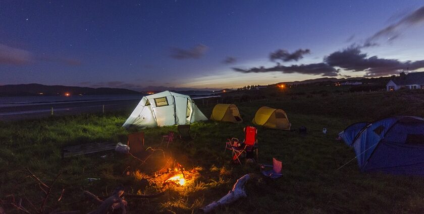 Bonfire and camping tents set up during the night with hills in the background.