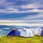 Several tents of blue and orange colour are placed next to each other on a hill